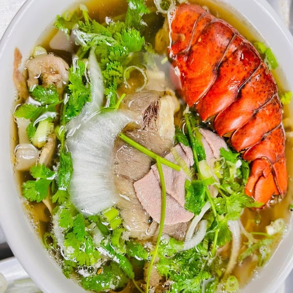 A bowl of The Phở Shop's Vietnamese pho with beef, herbs, and a large lobster tail.