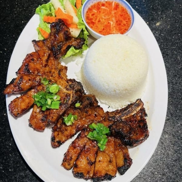 Vietnamese grilled pork chops with rice, pickled vegetables, and a dipping sauce on a white plate.