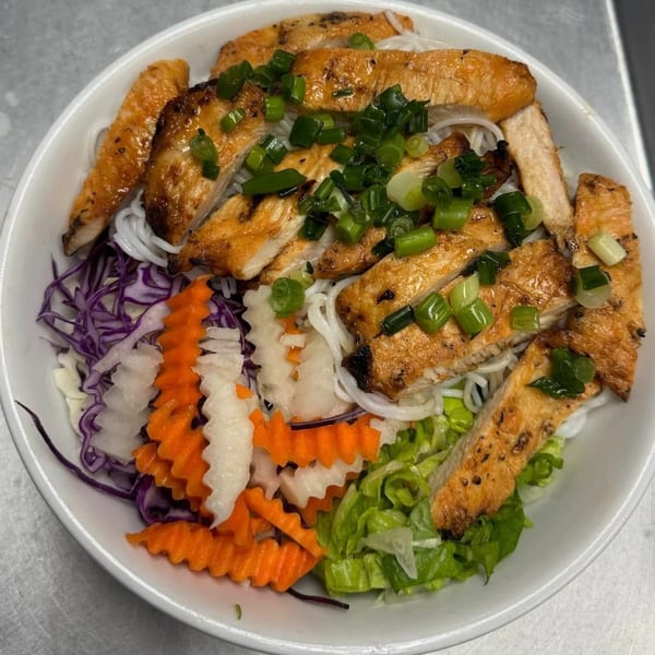 Vietnamese grilled chicken with vermicelli noodles, green onions, and pickled vegetables in a white bowl.