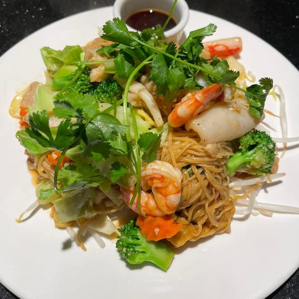 Vietnamese stir-fried noodles with shrimp, squid, broccoli, and cilantro, served with a side of sauce.