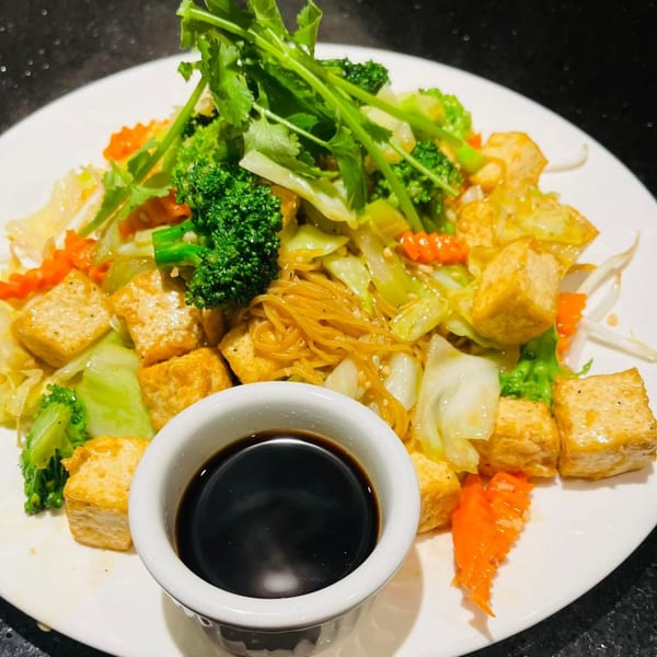 Vietnamese stir-fried noodles with tofu, broccoli, cabbage, carrots, and cilantro, with a side of sauce.