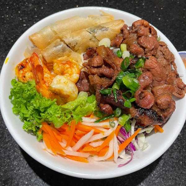 A Vietnamese vermicelli bowl with grilled beef, shrimp, crispy spring rolls, and fresh vegetables.