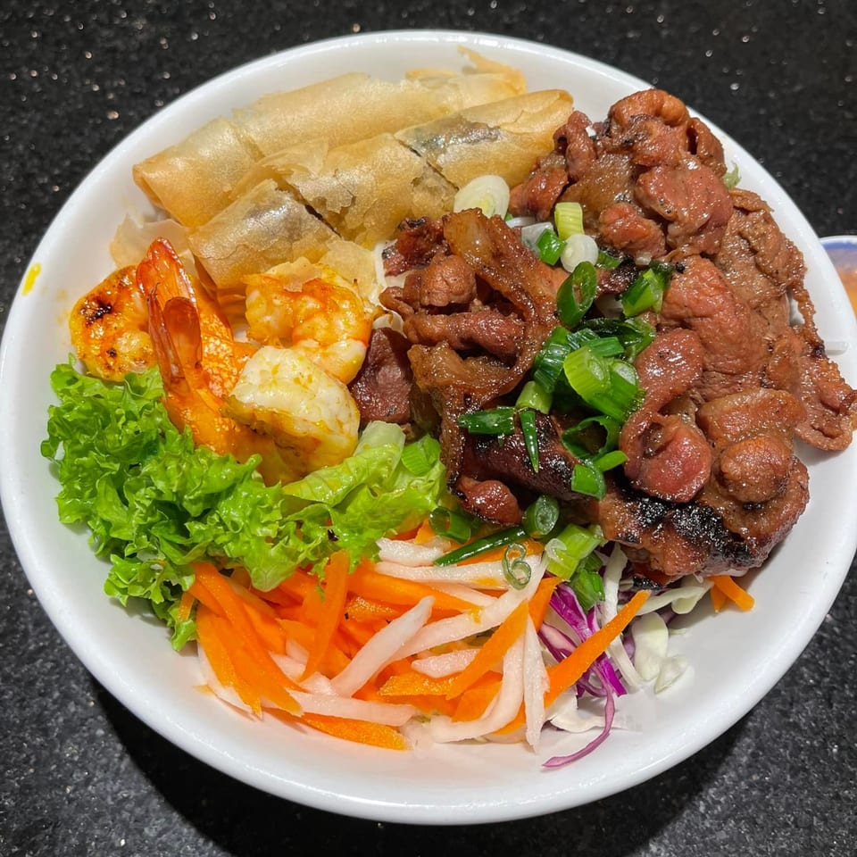 A Vietnamese vermicelli bowl with grilled beef, shrimp, crispy spring rolls, and fresh vegetables.