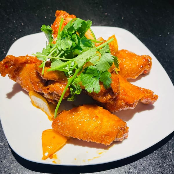Vietnamese chicken wings, glazed orange, topped with fresh cilantro, served on a white plate.