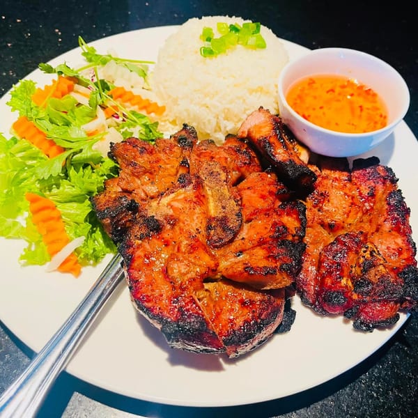 Grilled pork chops with rice, fresh salad, and a side of dipping sauce on a white plate.