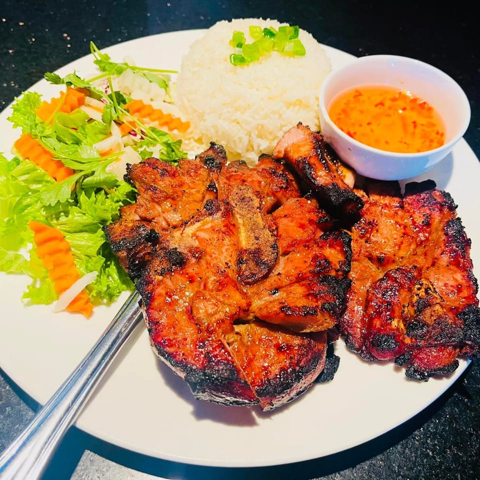 Grilled pork chops with rice, fresh salad, and a side of dipping sauce on a white plate.